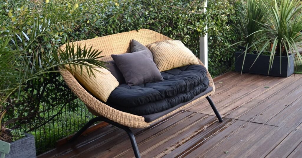 Comfortable stylish wicker sofa with soft seat and pillows placed in patio with lush green tropical vegetation in daytime